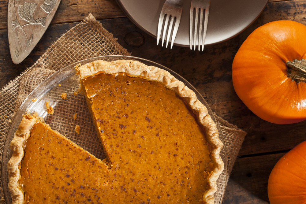 a pie dish with pumpkin pie and one slice taken out 