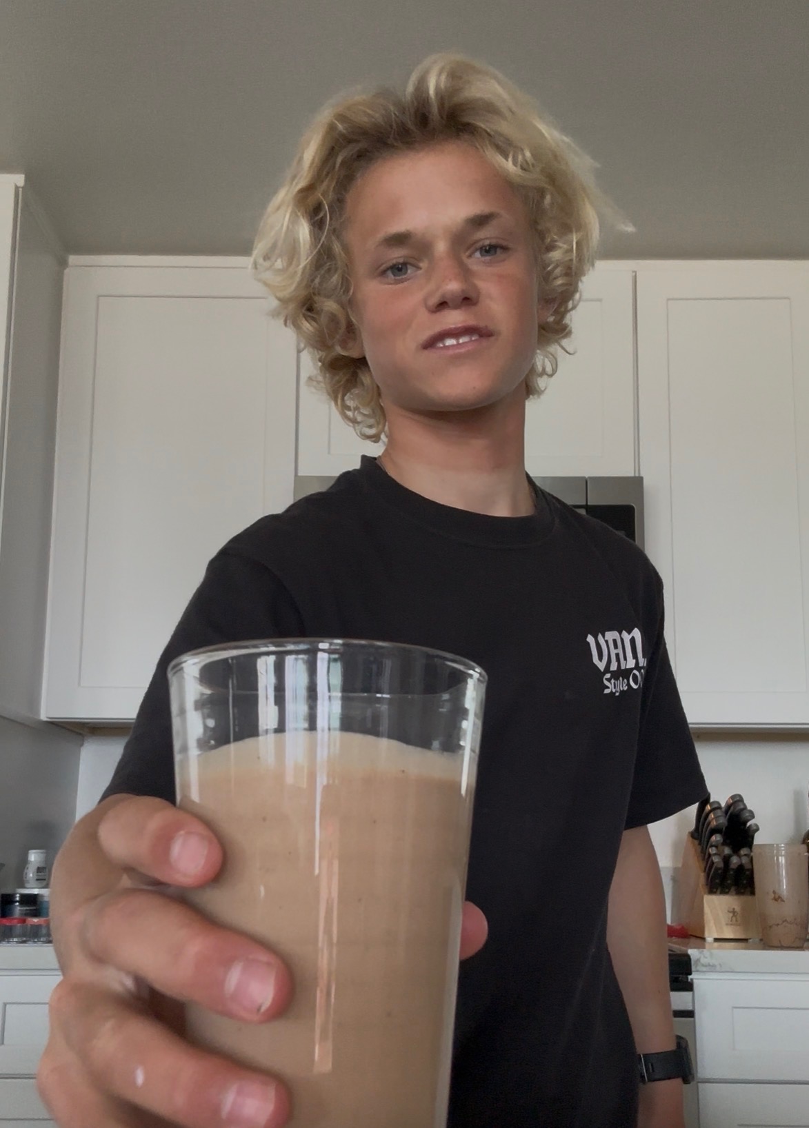 teenage boy smiling holding a tall glass filled with a chocolate smoothie