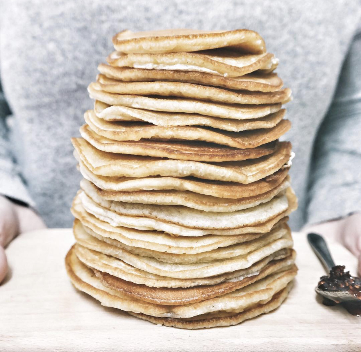 a giant stack of golden pancakes being held by a woman