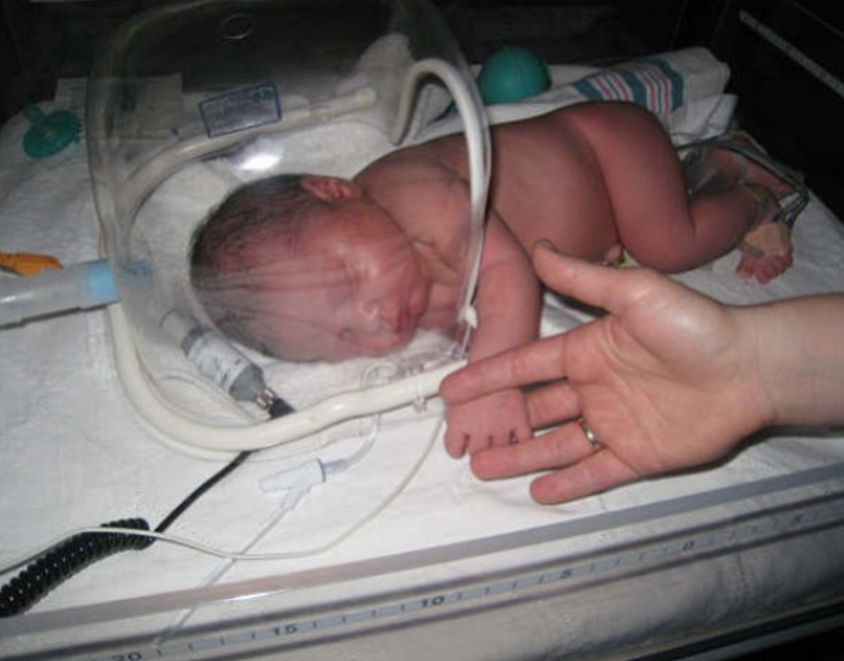 newborn baby in hospital under an incubator holding the moms fingers