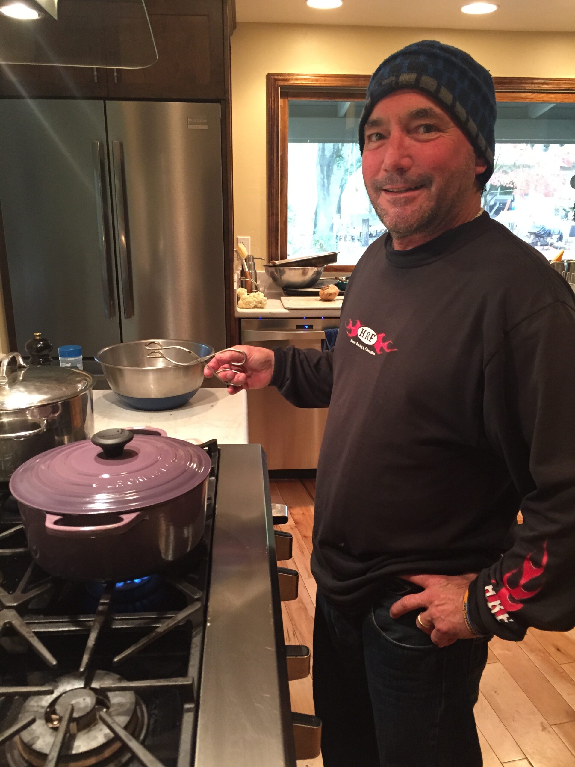 dad in the kitchen smiling cooking with an eggplant colored dutch oven