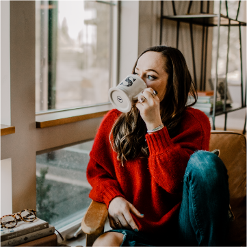 girl in red sweater drinking coffee looking out a window