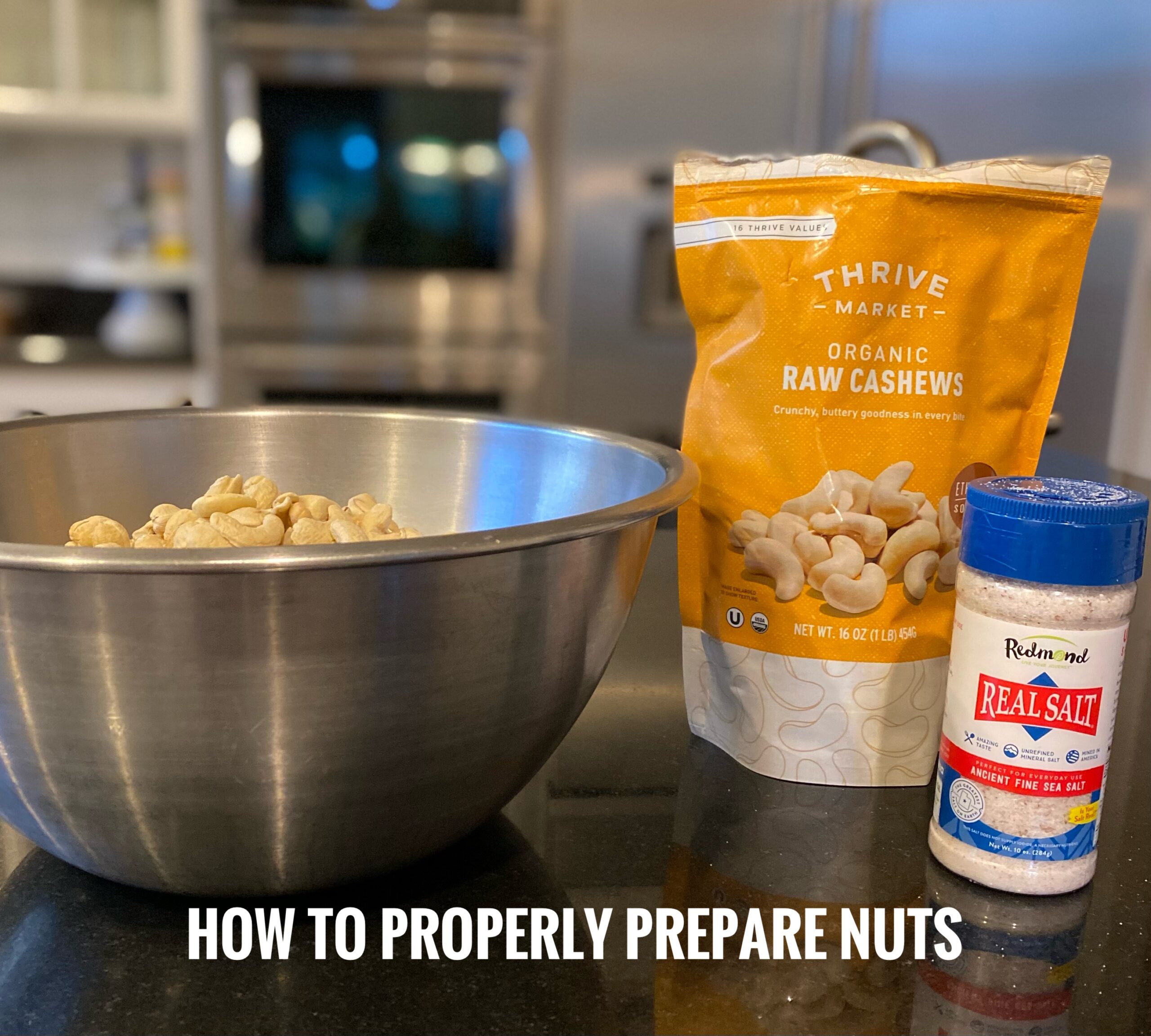 Bowl of cashews on the counter with a bag of organic cashews and a bottle of real sea salt